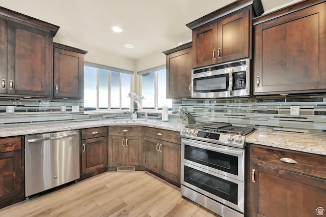 kitchen featuring tasteful backsplash, light wood finished floors, appliances with stainless steel finishes, and light stone countertops