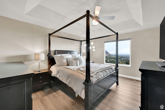 bedroom featuring a tray ceiling, light wood-style flooring, baseboards, and ceiling fan
