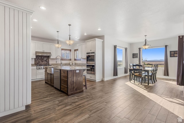 2409 W Rim Rock Dr, Stockton, UT 84071 - kitchen featuring a center island with sink, a kitchen breakfast bar, dark wood-style floors, stainless steel appliances, and decorative backsplash