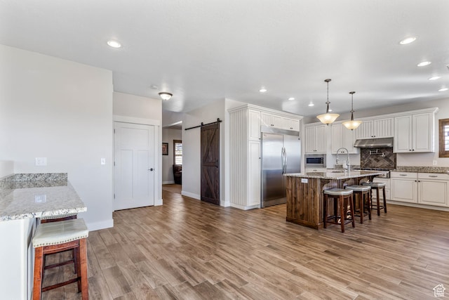 2409 W Rim Rock Dr, Stockton, UT 84071 - kitchen featuring light wood-style flooring, built in appliances, under cabinet range hood, a barn door, and a kitchen breakfast bar