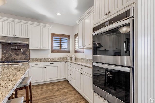 2409 W Rim Rock Dr, Stockton, UT 84071 - kitchen with light wood finished floors, backsplash, under cabinet range hood, white cabinets, and stainless steel appliances
