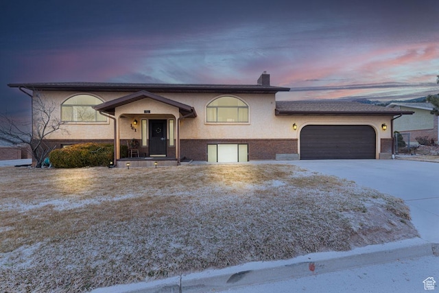 split foyer home with stucco siding, brick siding, concrete driveway, and a chimney