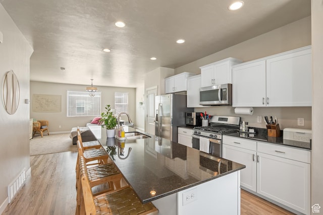kitchen featuring a sink, an island with sink, stainless steel appliances, white cabinetry, and visible vents
