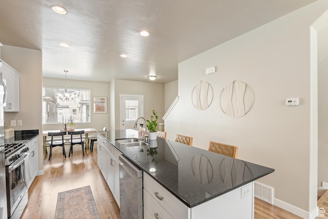 kitchen with appliances with stainless steel finishes, a sink, an island with sink, white cabinetry, and light wood-type flooring