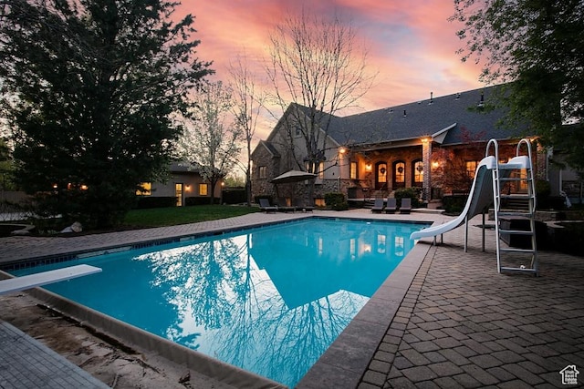 outdoor pool featuring a water slide, a patio, and a diving board