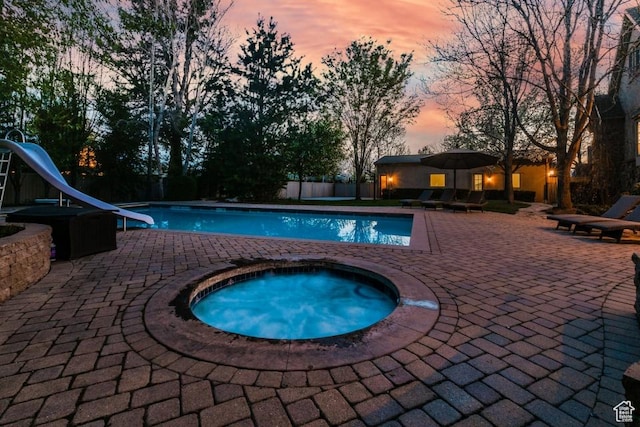 pool with a patio area, an in ground hot tub, a water slide, and fence