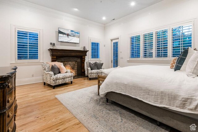 bedroom featuring crown molding, baseboards, recessed lighting, a warm lit fireplace, and light wood-style floors