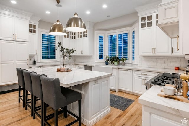 kitchen featuring a kitchen bar, white cabinets, light wood-style flooring, and light stone countertops