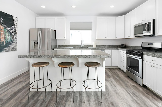 kitchen featuring a center island, stainless steel appliances, light wood-style floors, a breakfast bar area, and baseboards