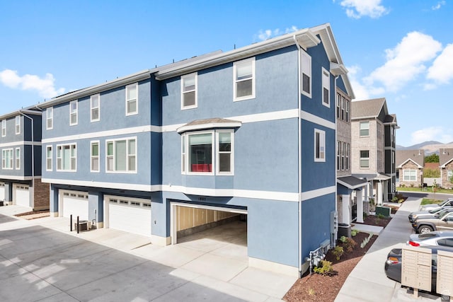 exterior space featuring concrete driveway, a garage, a residential view, and stucco siding