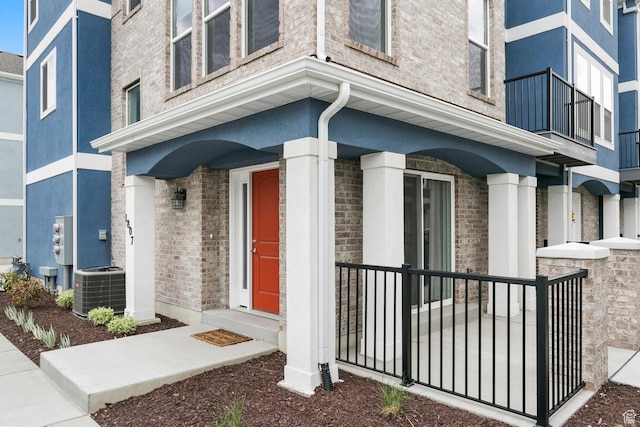 property entrance with brick siding, stucco siding, and cooling unit