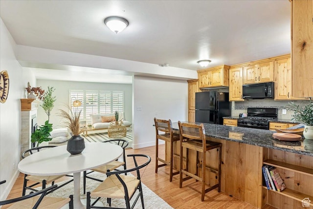 kitchen featuring light wood finished floors, backsplash, dark stone counters, a kitchen breakfast bar, and black appliances