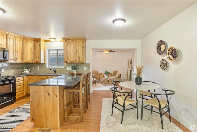 kitchen featuring a breakfast bar, light brown cabinets, a sink, black gas stove, and decorative backsplash