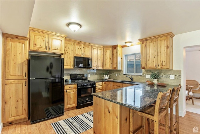 kitchen with dark stone counters, a peninsula, a sink, black appliances, and a kitchen bar