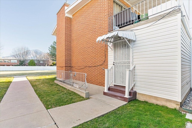 view of side of home featuring a yard, a mountain view, brick siding, and a balcony