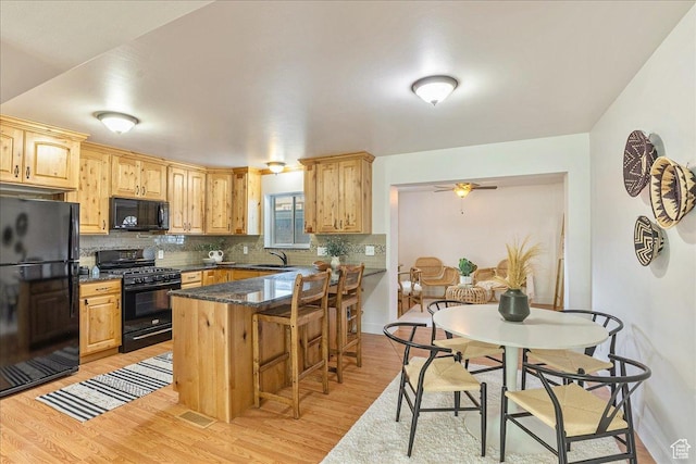 kitchen featuring a kitchen breakfast bar, backsplash, black appliances, and light wood-style flooring