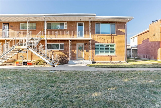 townhome / multi-family property with brick siding, stairs, and a front lawn