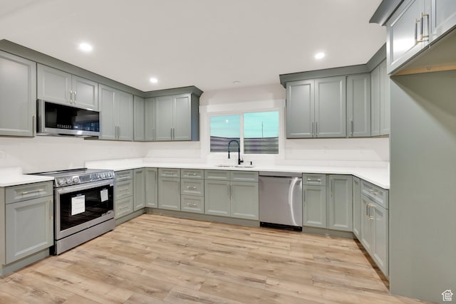 kitchen featuring appliances with stainless steel finishes, gray cabinetry, a sink, and light wood-type flooring
