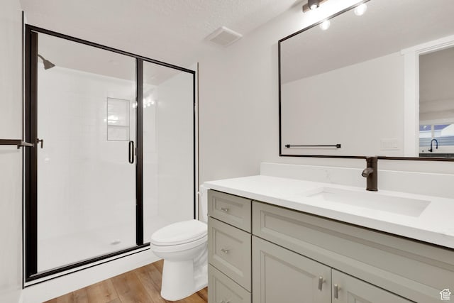 bathroom with wood finished floors, a stall shower, vanity, toilet, and visible vents