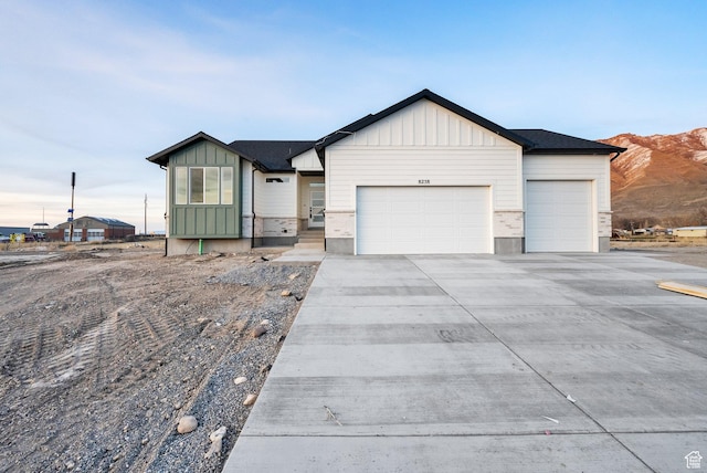 single story home with board and batten siding, concrete driveway, a garage, and a mountain view