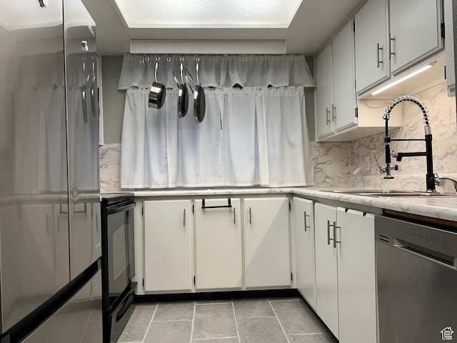 kitchen with decorative backsplash, light countertops, stainless steel appliances, white cabinetry, and a sink