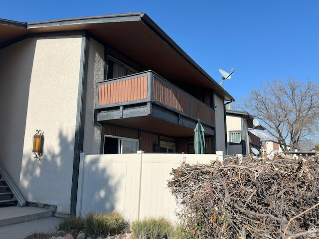 view of side of property with a balcony, stucco siding, and fence