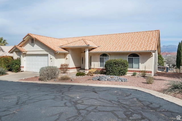 mediterranean / spanish home featuring stucco siding, driveway, an attached garage, and a tile roof
