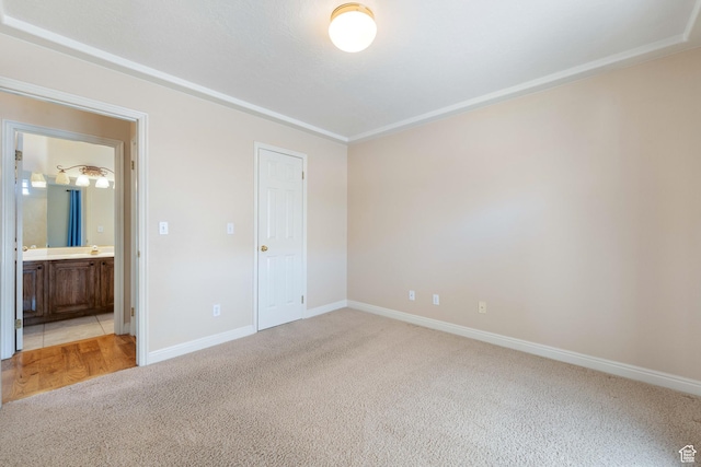 unfurnished bedroom featuring ensuite bath, light colored carpet, and baseboards