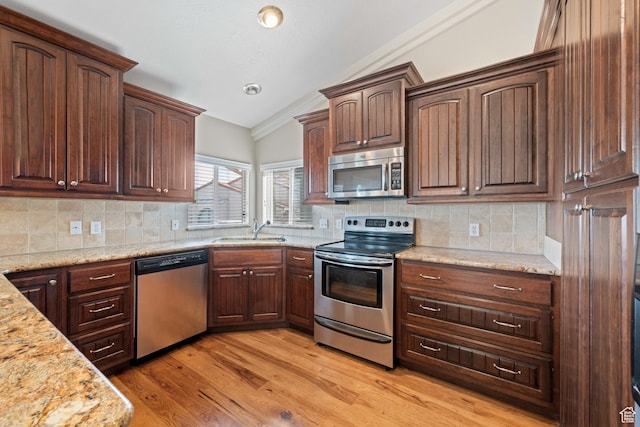 kitchen with light wood-style flooring, a sink, light stone counters, appliances with stainless steel finishes, and vaulted ceiling