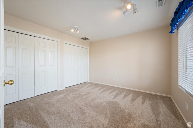 unfurnished bedroom featuring visible vents, carpet flooring, two closets, and baseboards