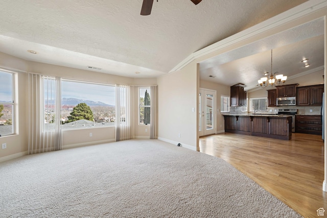 unfurnished living room with baseboards, a textured ceiling, ceiling fan with notable chandelier, and vaulted ceiling