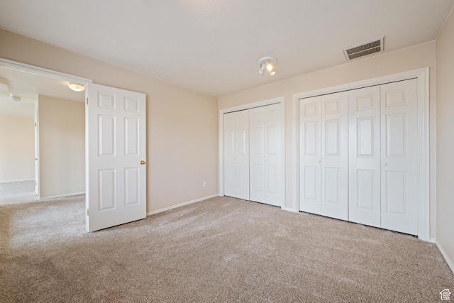 unfurnished bedroom with visible vents, carpet flooring, two closets, and baseboards