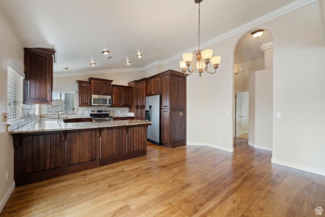 kitchen featuring light stone countertops, a peninsula, light wood-style floors, appliances with stainless steel finishes, and a chandelier