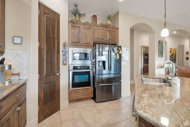 kitchen featuring a sink, light stone counters, arched walkways, appliances with stainless steel finishes, and light tile patterned floors