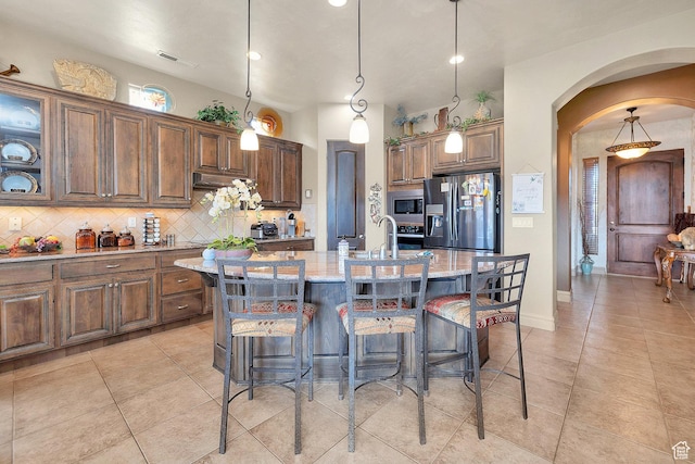 kitchen with arched walkways, backsplash, stainless steel appliances, and a breakfast bar
