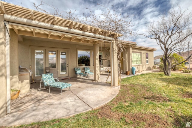 rear view of property with stucco siding, a lawn, a pergola, and a patio area