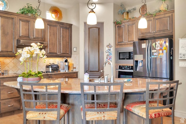 kitchen featuring light stone counters, a breakfast bar, stainless steel appliances, decorative backsplash, and under cabinet range hood