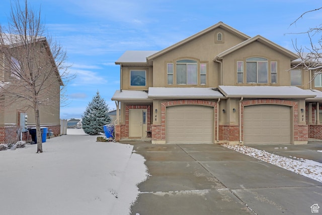view of front of home with brick siding, stucco siding, an attached garage, and driveway