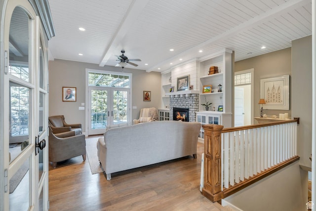 living area with beamed ceiling, a ceiling fan, wood finished floors, french doors, and a fireplace