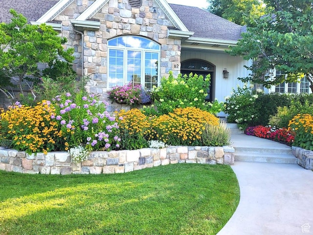 doorway to property with stone siding, a shingled roof, and a yard