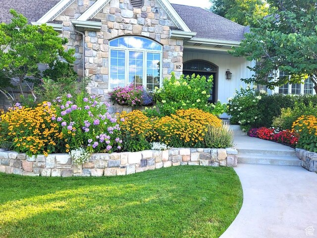 entrance to property with a yard, stone siding, and a shingled roof