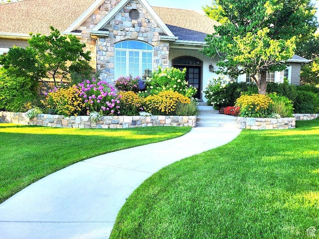 view of front of house with stone siding, a front lawn, and roof with shingles