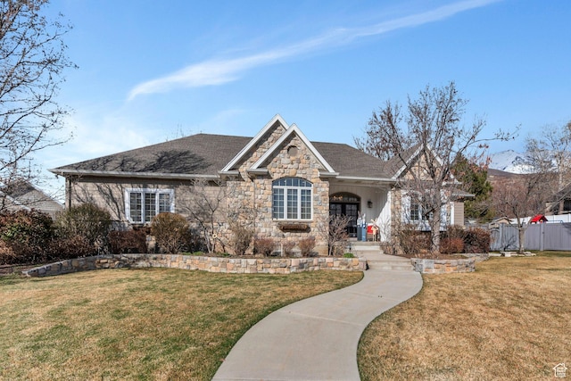 view of front facade featuring stone siding, a shingled roof, a front lawn, and fence