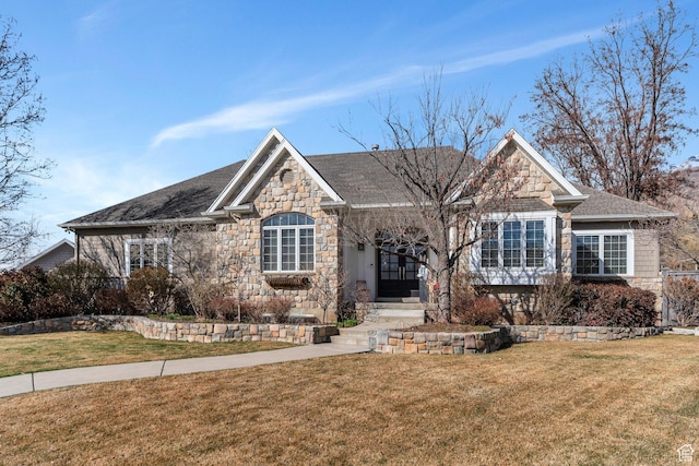 view of front of home featuring stone siding, a front lawn, and a shingled roof