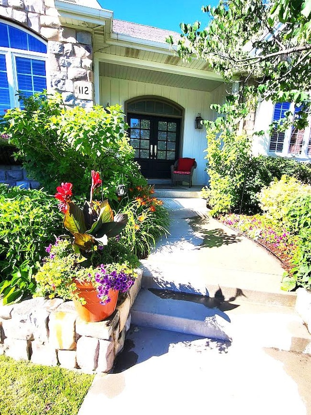 view of exterior entry featuring stone siding, covered porch, and french doors