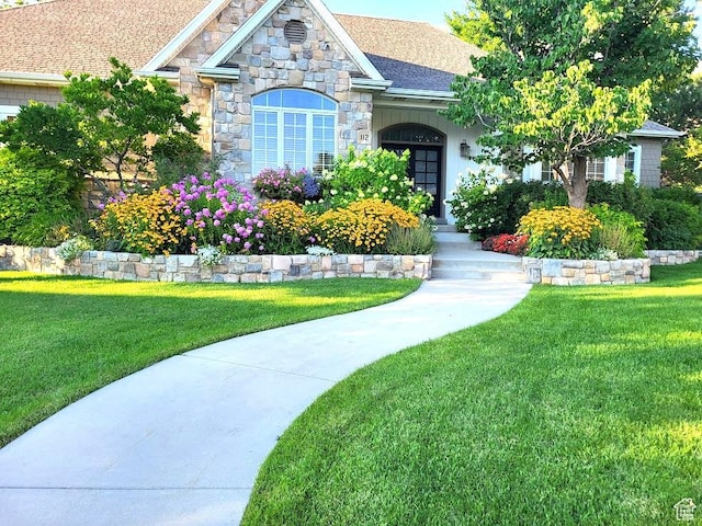 view of front of property featuring a front lawn, stone siding, and roof with shingles