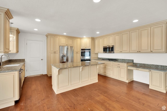 kitchen with a sink, cream cabinets, wood finished floors, appliances with stainless steel finishes, and stone counters