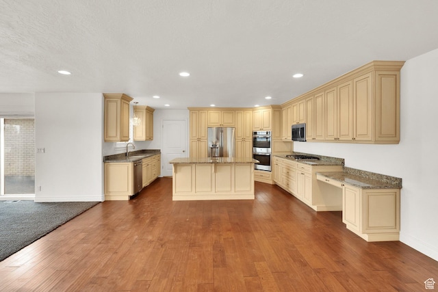 kitchen featuring dark stone countertops, wood finished floors, a sink, appliances with stainless steel finishes, and a center island