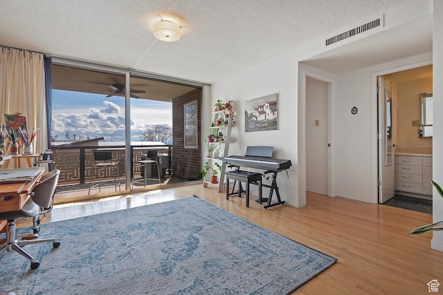 office area featuring expansive windows, wood finished floors, baseboards, visible vents, and a textured ceiling