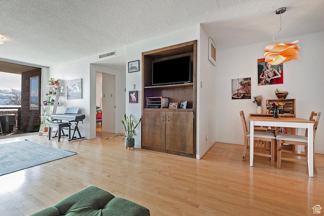 living room featuring expansive windows, visible vents, light wood finished floors, and a textured ceiling